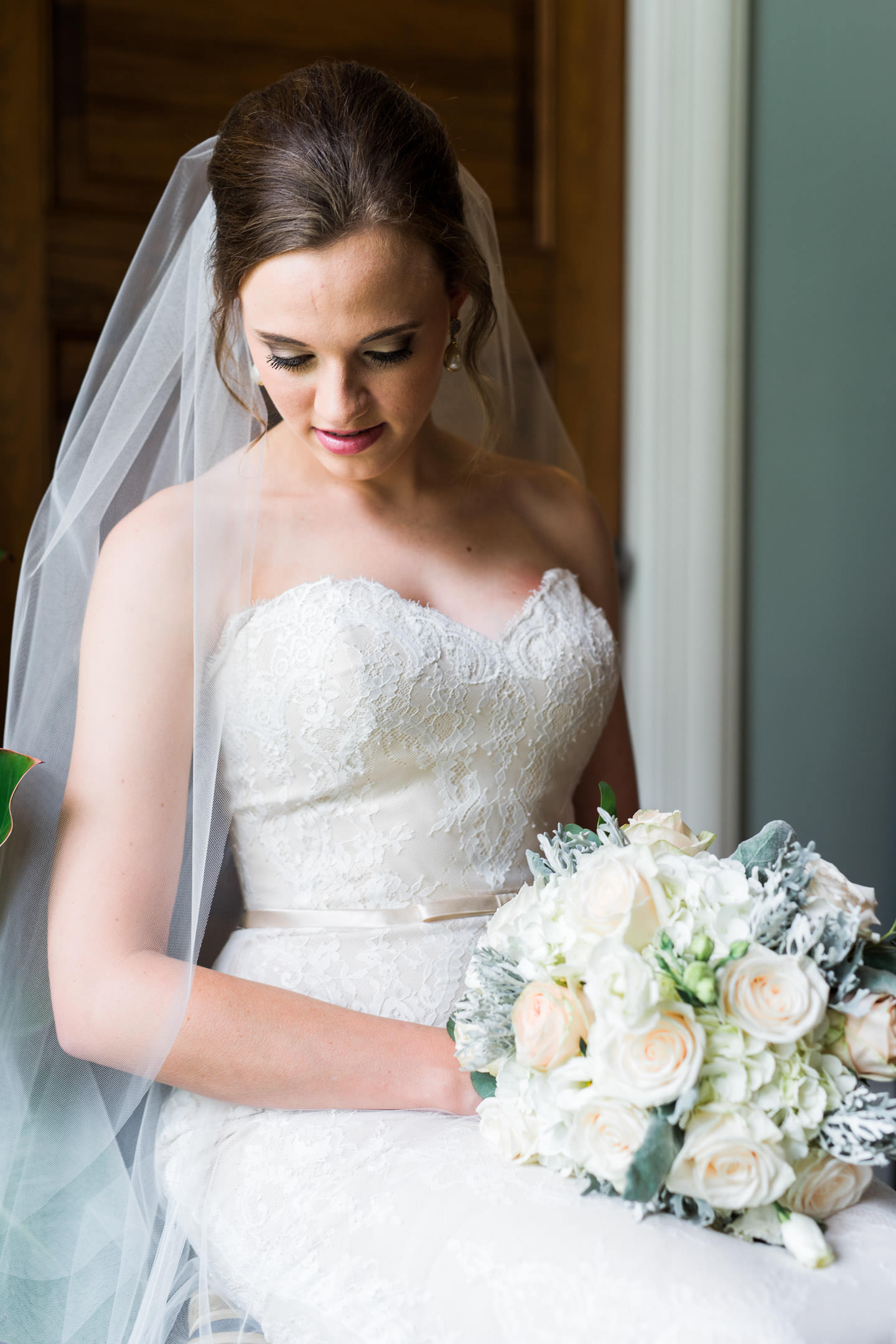 Elegant indoor portrait of bride sitting and looking at her dress inside Mississippi's best wedding venue