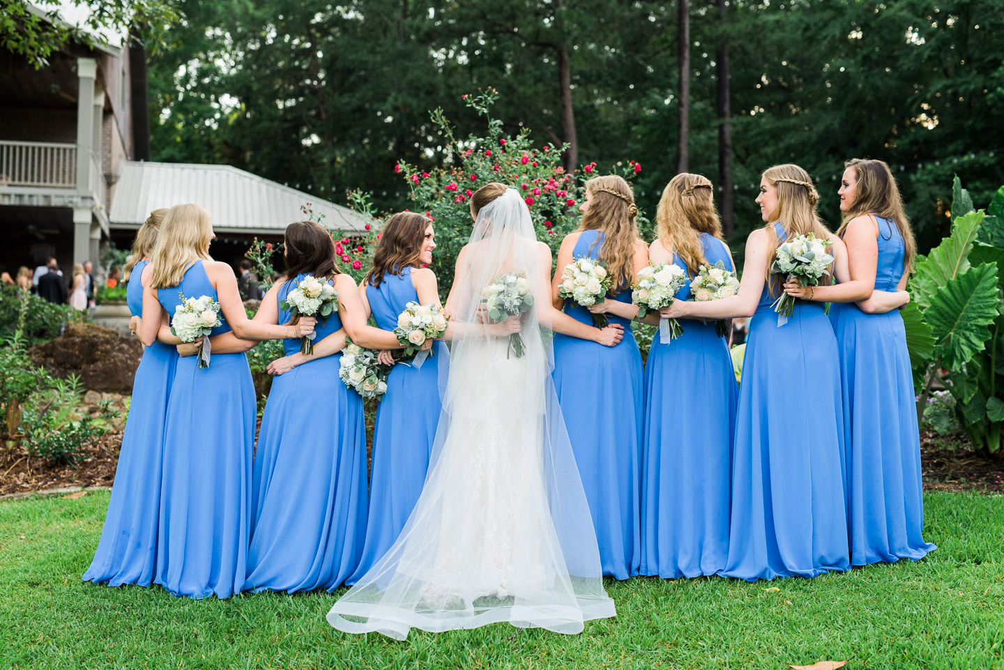 Outdoor fine art portrait of Bridesmaids with arms and bouquets around each other in front of Mississippi's best wedding venue