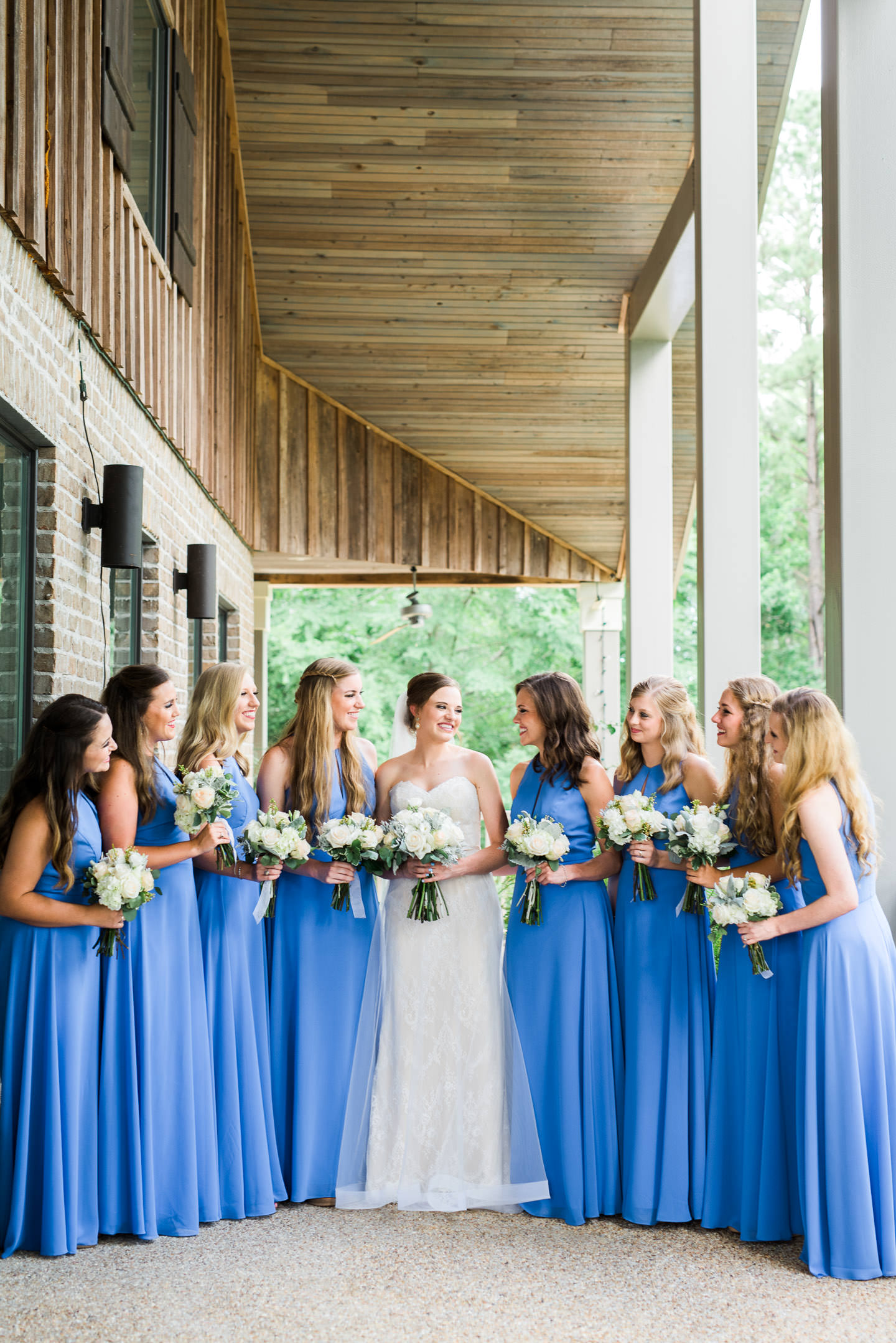 Mississippi bride and bridesmaids smiling at each other in blue long dresses and floral bouquets during their Southern wedding