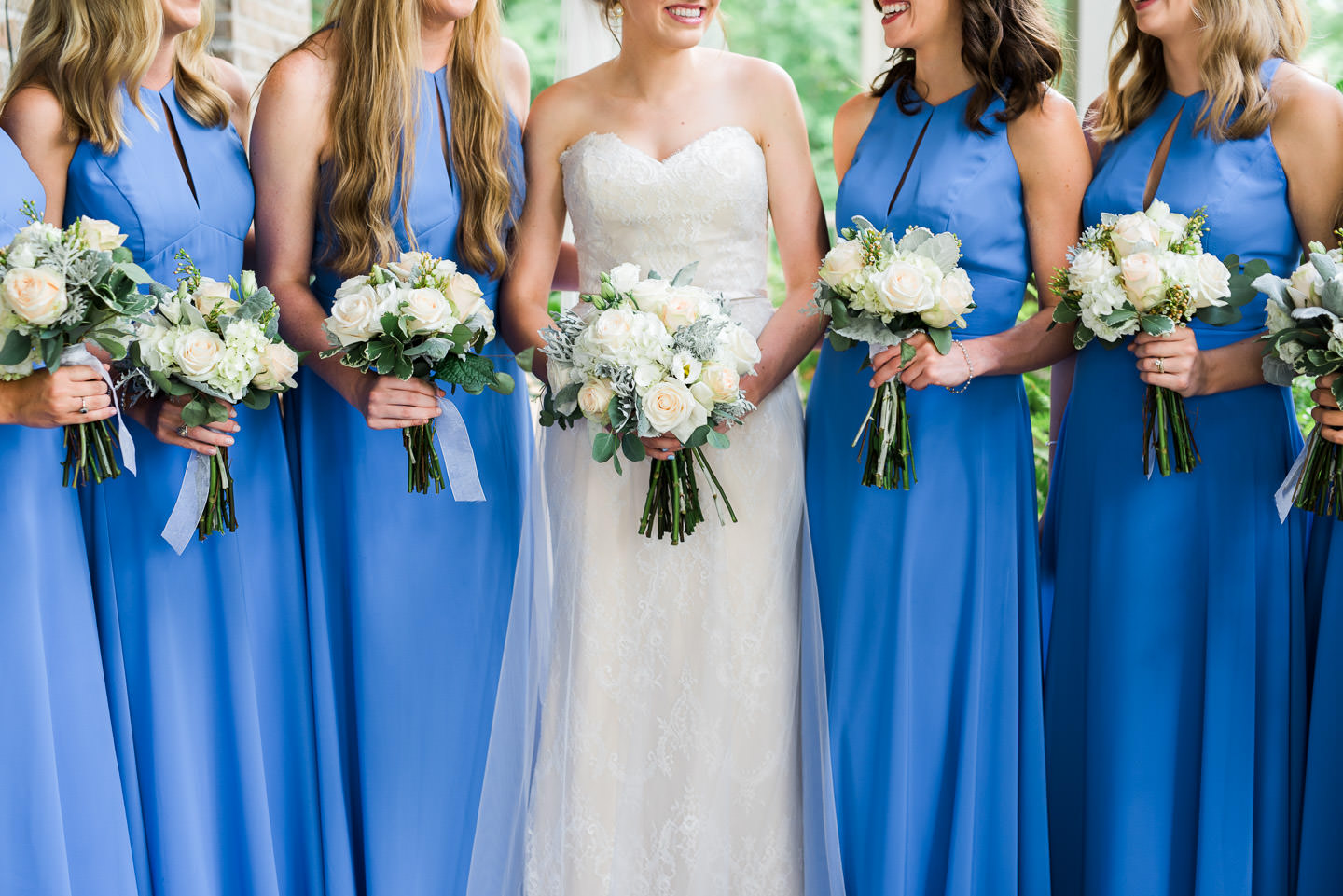 Detail photo of Southern Bridesmaids wearing long blue dresses with floral bouquets of white and peach roses, eucalyptus, dusty miller, and hydrangeas. 