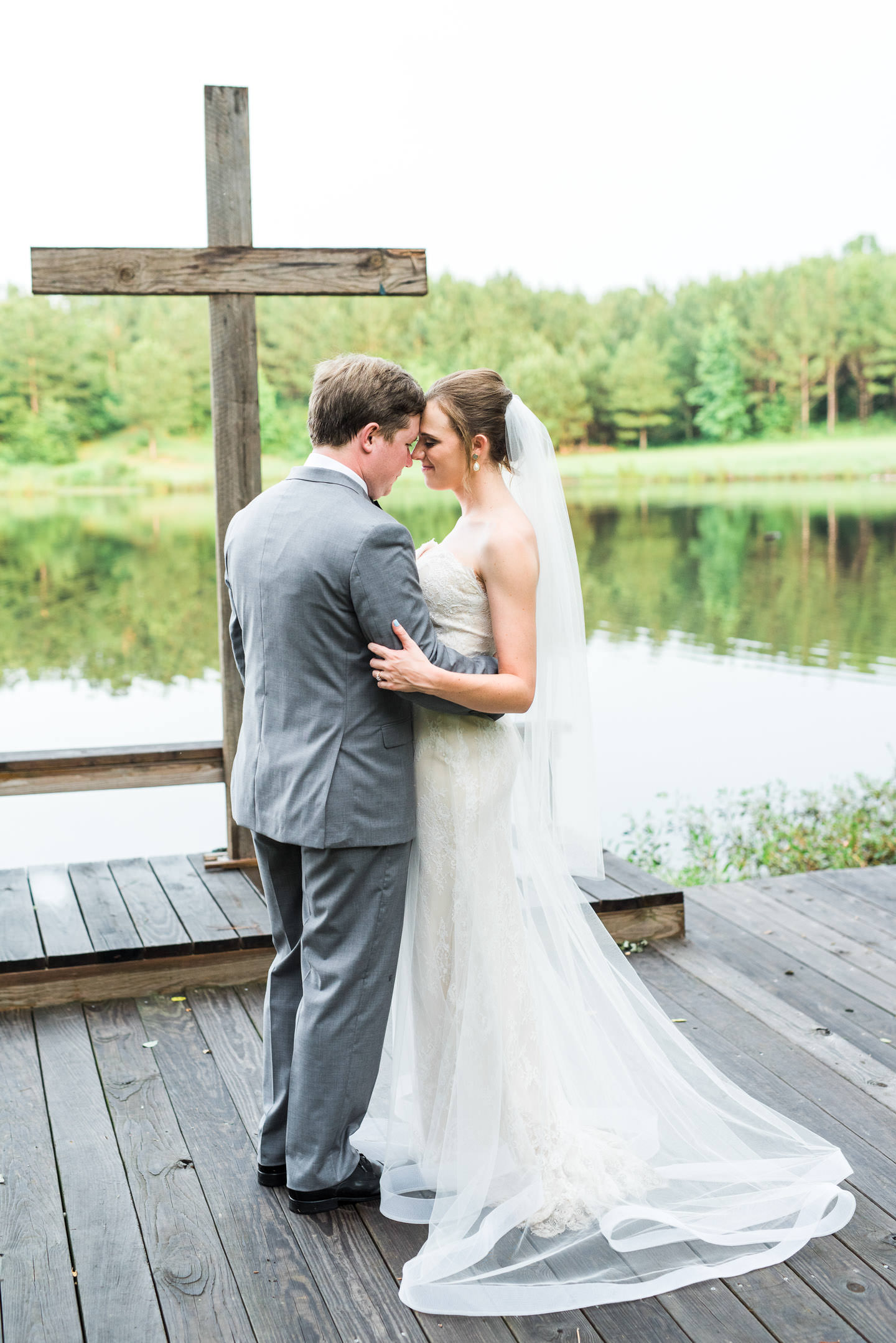 Serene portrait of Bride and Groom hugging in front of lake following their Mississippi outdoor wedding ceremony