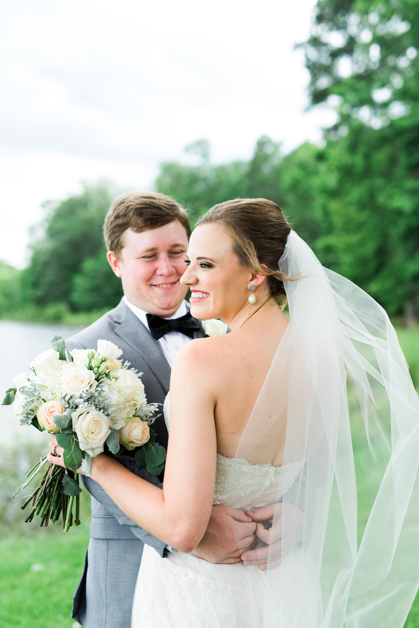 Joyful portrait of southern bride smiles while groom looks at her before their outdoor Mississippi wedding