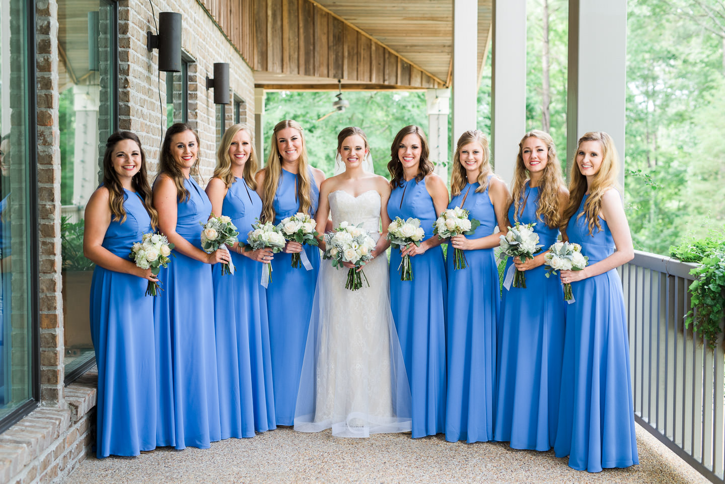 Southern bride with bridesmaids wearing long blue dresses with neutral floral bouquets of eucalyptus, dusty miller, hydrangeas, and peach roses during Mississippi wedding