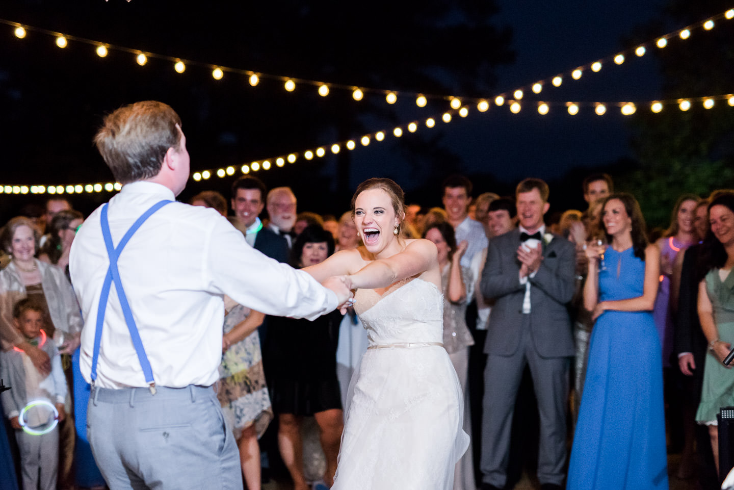 Bride and groom's joyful first dance under cafe lights while guests watch during Jackson, Mississippi outdoor wedding reception
